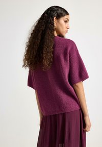 Maglione oversize a maniche corte in viola profondo, realizzato in un tessuto morbido e testurizzato. Presenta una vestibilità rilassata e un'orlo che arriva alla vita.