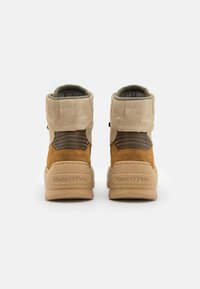 Zapatillas altas de ante marrón y tostado con suelas de goma, cuellos acolchados y forro interior verde. Presentan una marca en el talón.