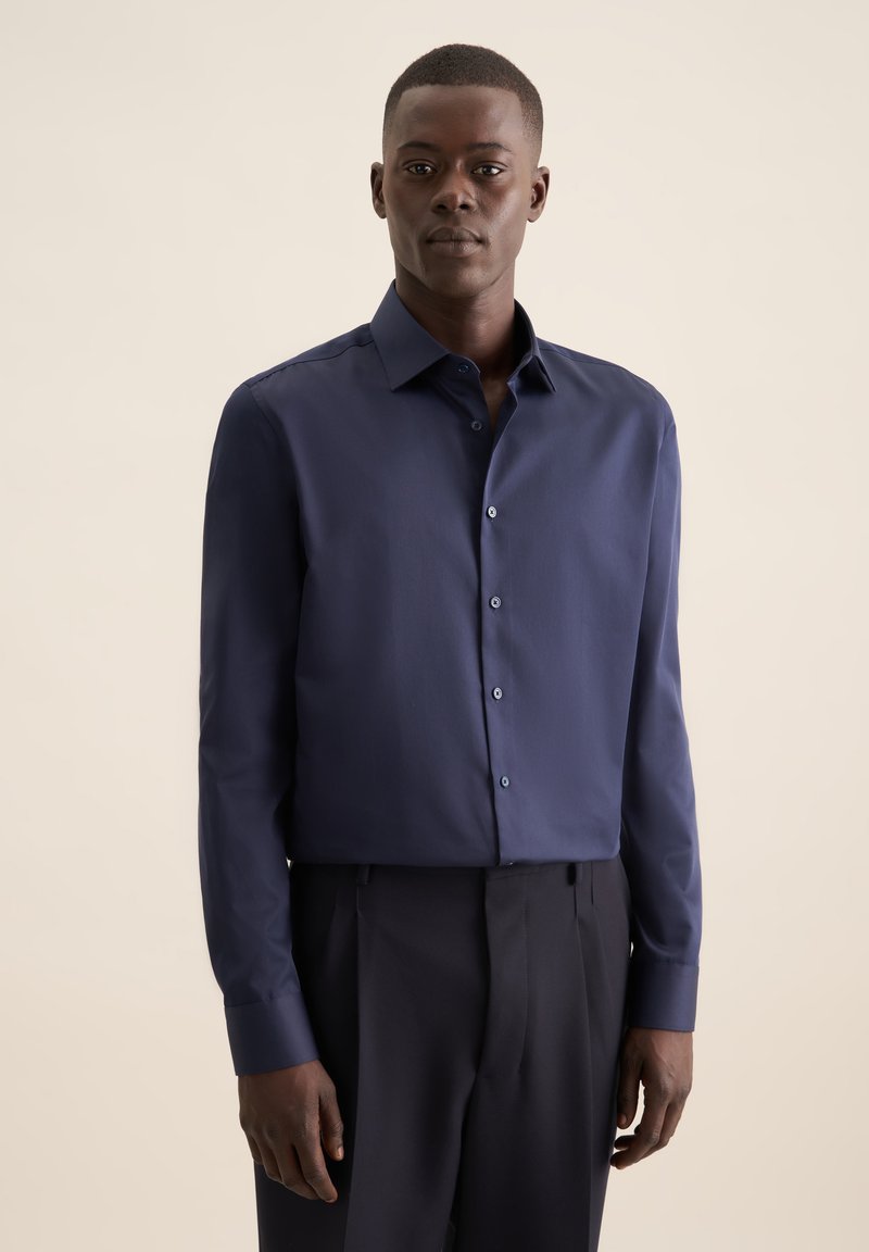 Navyblauwe overhemd met lange mouwen van een gladde stof, voorzien van een klassieke kraag, knoopsluiting aan de voorkant en een getailleerd ontwerp. Gecombineerd met donkere broeken.