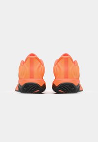 Neon orange athletic shoes with a wave-like design and black rubber soles. Features a textured upper and flat heel.