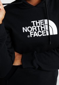 Felpa nera con cappuccio realizzata in misto cotone, con logo bianco sulla parte anteriore. Include una tasca frontale e cappuccio regolabile con coulisse.
