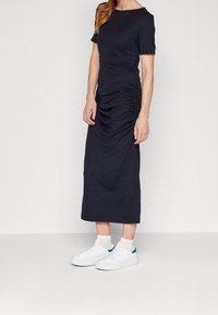 Abito midi blu navy realizzato in tessuto elasticizzato, con maniche corte e dettagli arricciati ai lati, abbinato a sneakers bianche.