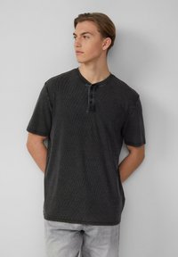 Schwarzes T-Shirt mit kurzen Ärmeln, runder Halslinie und Knopfleiste mit drei Knöpfen. Weicher, strukturierter Stoff mit dezentem Rippdesign und lockerer Passform.