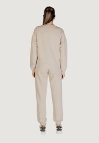 Felpa beige con pantaloni coordinati, caratterizzati da polsini a costine e una vestibilità rilassata, abbinati a scarpe con motivo e un alto codino.