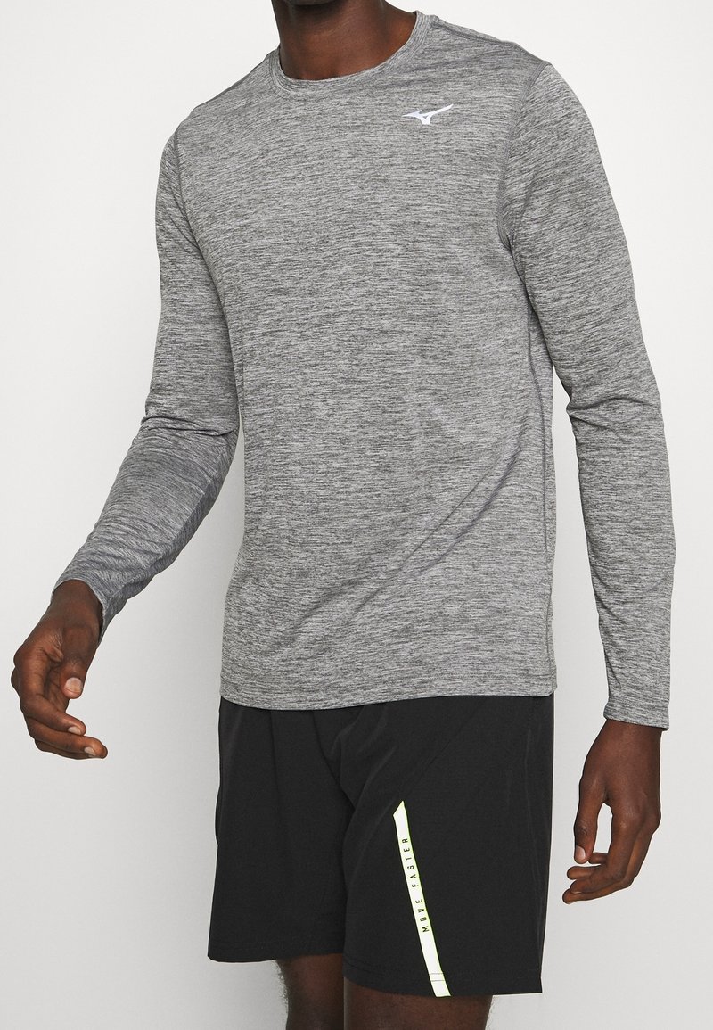 Langärmliges, graues Sportshirt mit strukturiertem Finish und einem weißen Logo auf der Brust, kombiniert mit schwarzen Shorts mit einem gelben Akzentstreifen.