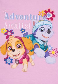 Rosa Grafik-T-Shirt mit zwei Cartoon-Hunden, einer im rosa Outfit und der andere in einer blauen Jacke, mit floralen Akzenten und dem Text "Abenteuer wartet!"