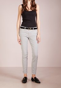 Svart ärmlös topp, ljusgrå slim-fit jeans, svart bälte med gul cirkelspänne, svarta loafers. Slät tyg, minimal mönster, avslappnad design.