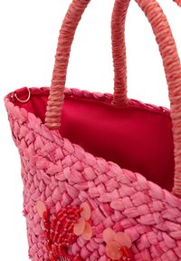 Rosa vävd väska med en slät, röd innerfoder. Har flätade handtag och dekorativa blomsterdetaljer gjorda av pärlor och blad.