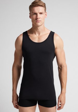 Schwarzes Tanktop aus glattem Stoff mit rundem Ausschnitt und breiten Trägern, getragen mit passenden schwarzen Shorts.