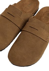 Scarpe slip-on marroni in suede con una larga cinghia sulla parte superiore. Superficie texture e forma della punta curvata. Suola piatta con dettagli di cucitura sottili.