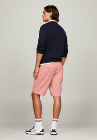 Suéter navy con mangas arremangadas, combinado con pantalones cortos rosas. Los pantalones cortos tienen presillas para cinturón y un bolsillo trasero. Zapatillas deportivas blancas con acentos.