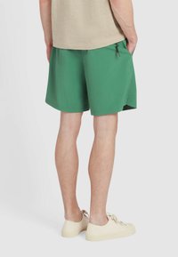 Pantaloni corti verdi realizzati in un tessuto leggero con vita elastica, tasche laterali e cordoncino. Abbinati a scarpe chiare.