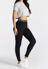 Sorte leggins med en SIKSILK-logo i taljen, parret med en grå cropped t-shirt og hvide sneakers. Glat stof, tætsiddende design.