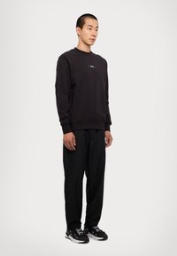 Felpa nera a girocollo con un'etichetta rettangolare sul petto, abbinata a pantaloni neri larghi e sneaker nere. Texture liscia, design casual.