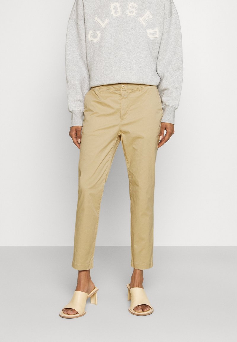 Chinos beiges coupe slim, en tissu léger. Associés à un sweat-shirt gris et des mules beiges à bout ouvert avec un talon bloc.