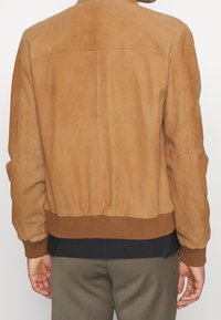 Hnědá semišová bomber bunda s žebrovaným pasem a manžetami, která má hladkou texturu a jednoduchý design. Zadní pohled ukazuje detaily šití.