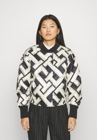 Padded bomber jacket in black, cream, and grey geometric pattern. Features ribbed cuffs and collar, snap closure, and glossy finish.