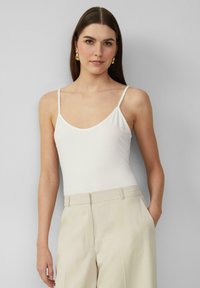 Witte spaghettiband bodysuit met een ronde hals, gemaakt van zachte stof, gecombineerd met hoge beige broeken. Eenvoudig en minimalistisch ontwerp.