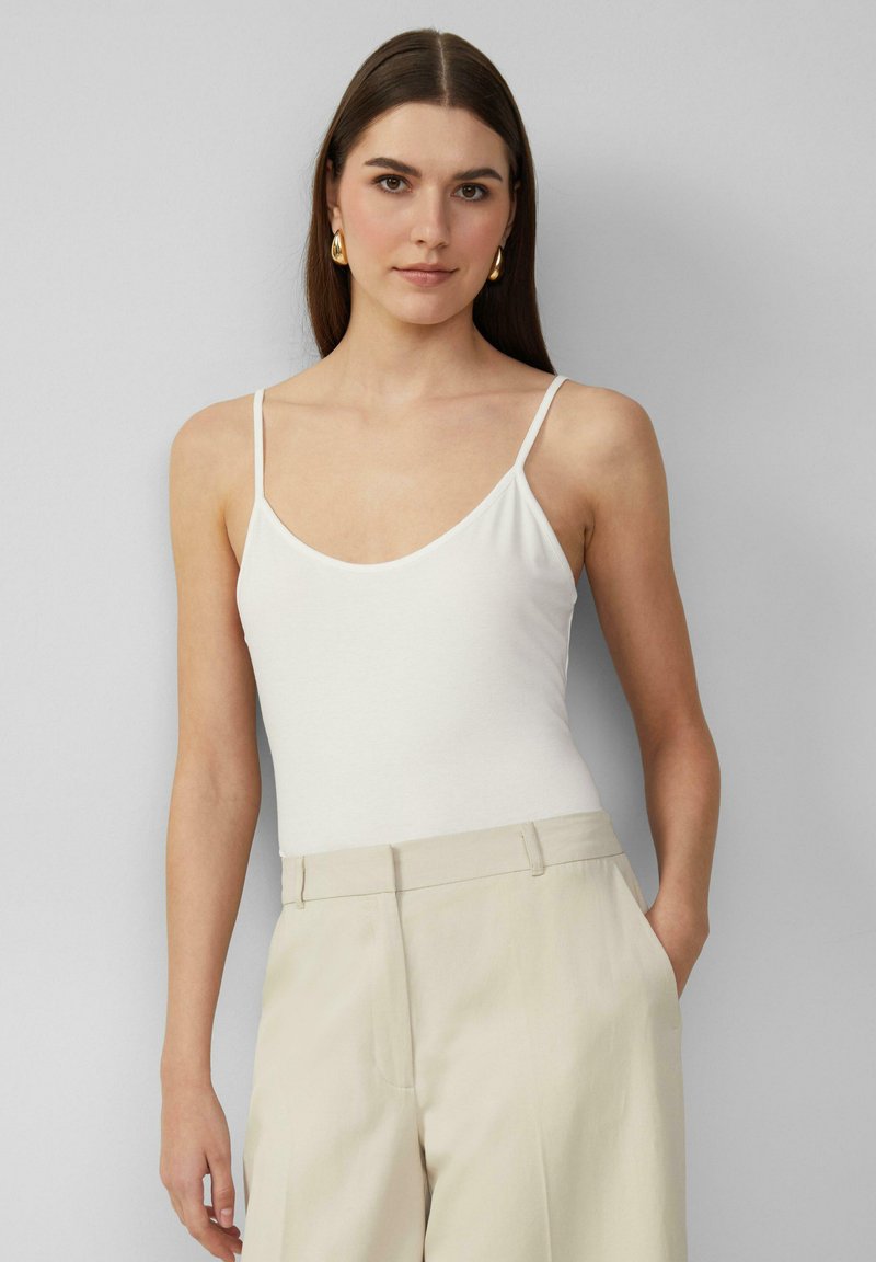 Witte spaghettiband bodysuit met een ronde hals, gemaakt van zachte stof, gecombineerd met hoge beige broeken. Eenvoudig en minimalistisch ontwerp.