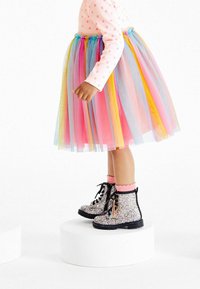 Flerfärgad tullekjol med rosa, blå och gula lager; matchad med glittriga svarta stövlar och rosa ankelsockor. Långärmad topp med prickar.