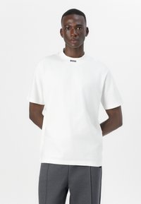 Tricou alb din bumbac cu mâneci scurte, având un decolteu rotund și logo-ul negru "BOSS" la guler. Textură netedă, croială lejeră.