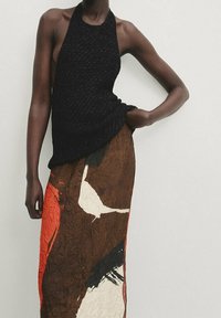 Top halter nero in maglia con una finitura testurizzata, abbinato a una lunga gonna stropicciata in toni caldi e motivi astratti.