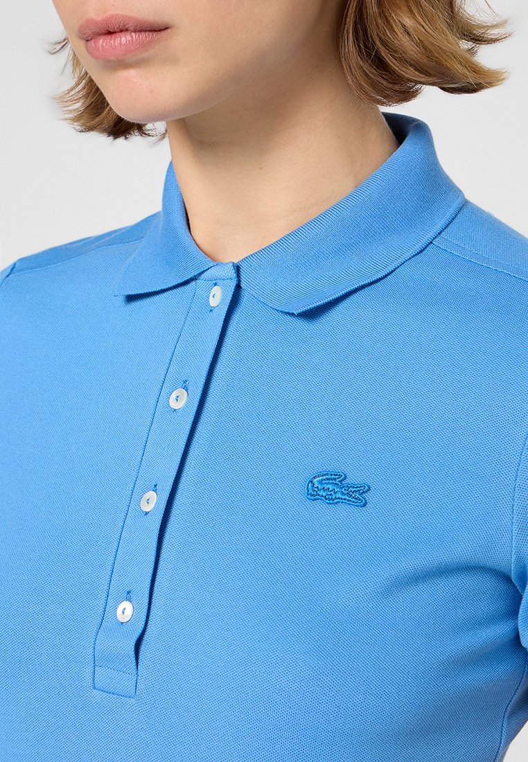 Polo bleu clair en coton texturé avec un col, patte de boutonnage à trois boutons et un logo brodé sur la poitrine gauche.