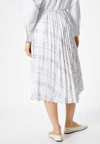 Jupe midi plissée blanche avec un motif vichy gris et lavande. Dotée d'une taille élastique, elle tombe en dessous du mollet. Associée à des chaussures plates.