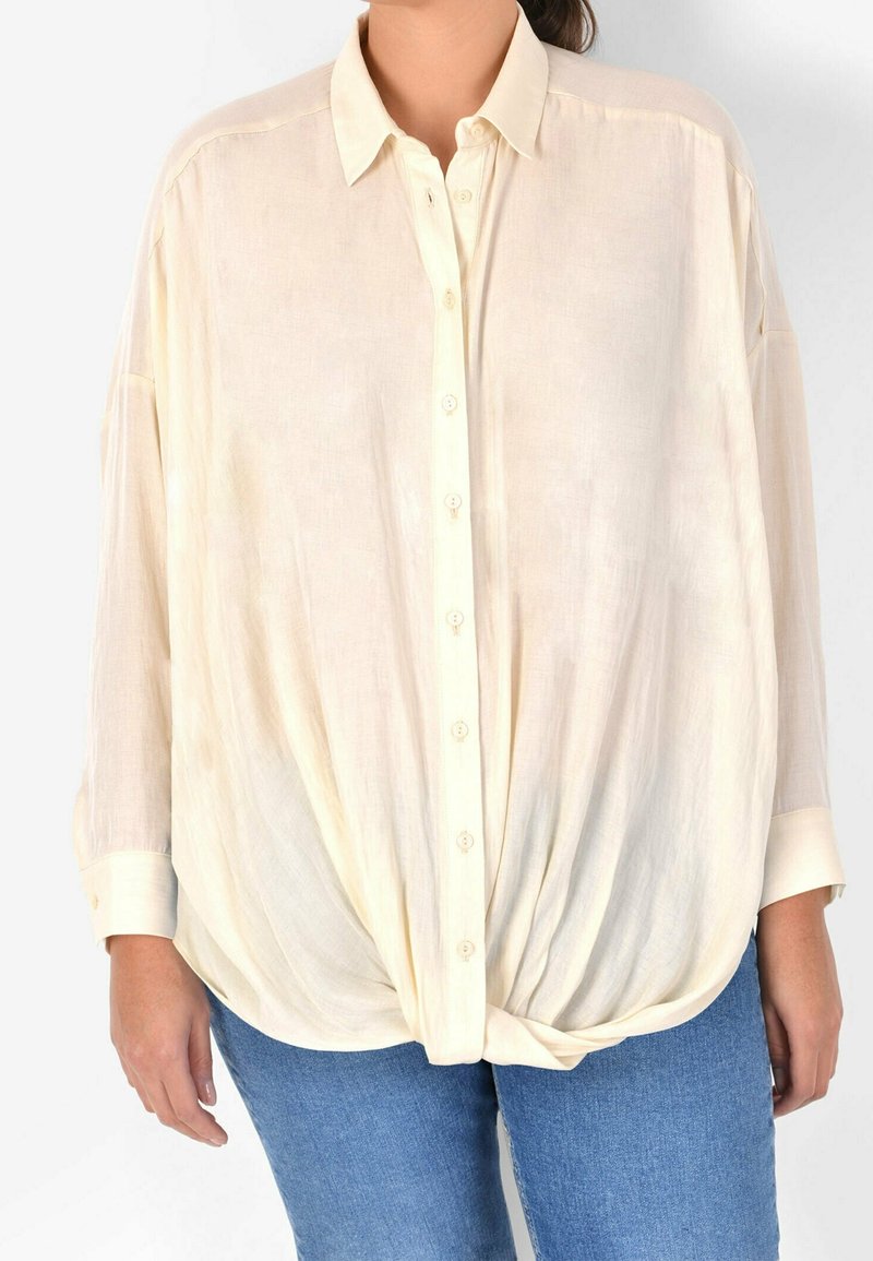 Cream-colored, lightweight button-up shirt with a collar, long sleeves, and a knotted front design. Made from a soft, sheer fabric.