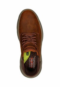 Zapato de cuero marrón con superficie texturizada, punta redonda y cordones marrones. Presenta una plantilla acolchada verde y negra con detalle de logo.
