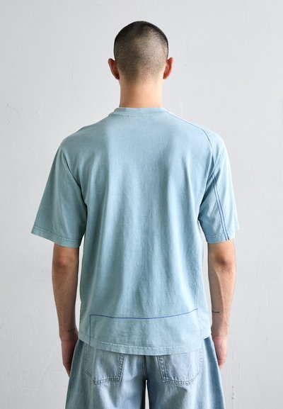 T-shirt en coton bleu clair à manches courtes, avec des détails de couture visibles et une coupe décontractée. Il présente un col rond et une texture douce.
