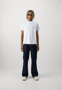 Hvit, t-skjorte med korte ermer kombinert med mørkeblå, løstsittende jeans og hvite joggesko. Tilbehøret inkluderer smale solbriller.