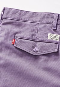 Pantaloni din corduroy lavandă cu dungi verticale, având un buzunar posterior cu închidere prin nasture și un etichetă Levi's pe talie.