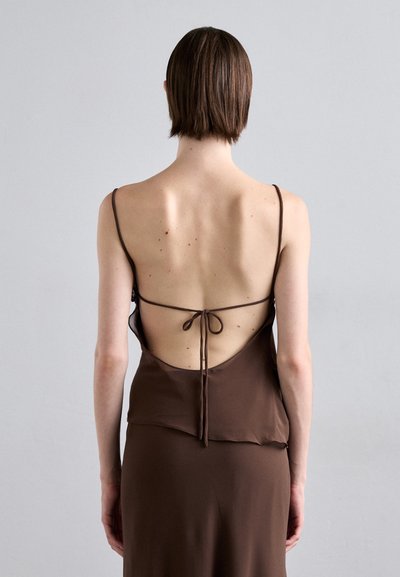 Bruine mouwloze jurk met open rug, zachte textuur, dunne bandjes en een strikdetail op de taille. Soepele, minimalistische vormgeving.