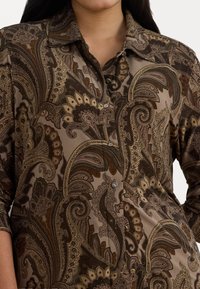 Ruda raštuota palaidinė su paisley raštais, mygtukų uždarymu ir apykakle. Audinys yra lygus su sudėtingais detalėmis.