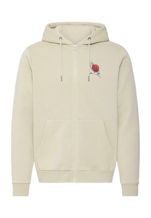 Sweat à capuche beige avec fermeture éclair, poches avant et un petit motif de grue en noir et rouge près de la poitrine gauche.