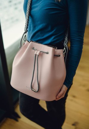 Pink leather bucket bag with a drawstring closure, gray braided strap, silver hardware accents, and a smooth texture.