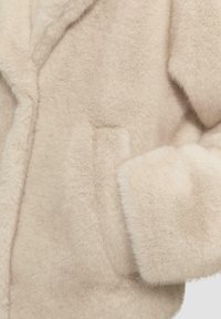 Faux fur jas in lichtbeige met een zachte, gestructureerde oppervlakte. Voorzien van een gekarteld kraag en een enkele zijzak voor extra detailing.