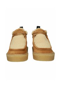 Scarpe scamosciate tan con fodera fluffy beige, design senza lacci e suole in gomma spesse e texturizzate. Brand nero sulle linguette del tallone.