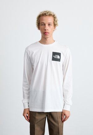 Langærmet hvid t-shirt med et sort firkantet logo på venstre bryst. Klassisk pasform, bomuldsmateriale, blødt tekstur, enkelt design.
