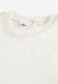 Cream-colored short-sleeve crew neck shirt, made of soft cotton, featuring ribbed neckband and contrasting stitching details.