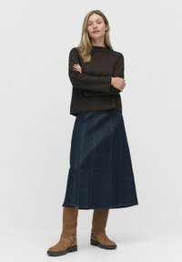 Brązowa bluzka z długim rękawem o prostym kroju, zestawiona z długą spódnicą z ciemnego denimu. Brązowe skórzane botki za kolano z klamrami. Prosty, nowoczesny design.