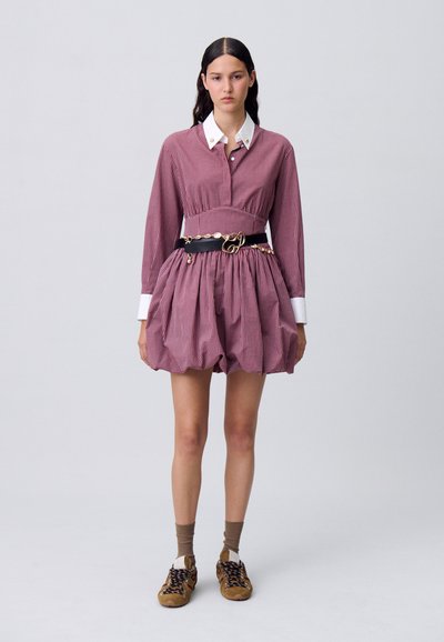 Una modella indossa un abito a righe con vita stretta e gonna ampia, abbinato a una cintura nera e sneakers casual.