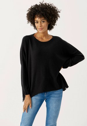 Black knit sweater with a relaxed fit, round neckline, and drop shoulders. Paired with blue denim jeans, featuring a smooth texture and side slits.