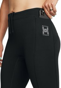 Leggings sportivi neri con vita regolabile tramite cordoncino, dotati di una tasca laterale per il telefono e di un logo Under Armour bianco sul lato.