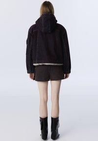 Tmavě modrá džínová bunda s kapucí, chlupatým podšívkou na spodním okraji a mírně zkráceným střihem. Stylizováno s hnědými šortkami a černými lesklými kotníkovými botami.