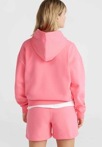 Felpa rosa con cappuccio, vestibilità comoda e polsini a costine, abbinata a pantaloni corti rosa coordinati. Il materiale sembra morbido e confortevole.