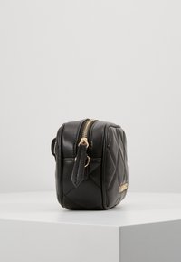 Svart kviltad läderväska med en guldfärgad dragkedja och hårdvara. Rektangulär form med ett litet handtag och slät yta.