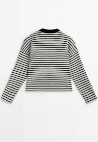 Pull en tricot avec des rayures horizontales noires et blanches, manches longues et un col rond noir, présentant un tissu texturé.