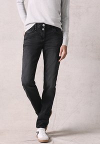 Donkerdenimjeans met een rechte pasvorm, voorzien van twee voorkruiken, knoopsluiting en een lichte versleten textuur. Gepaard met witte sneakers.